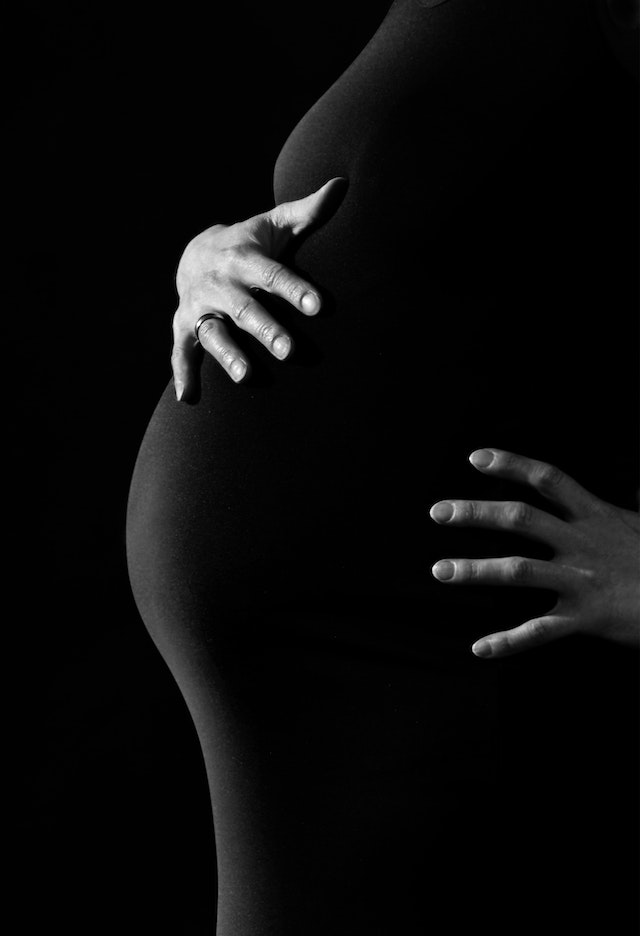Black-and-white photo of a pregnant woman's body in profile, showing hands on belly