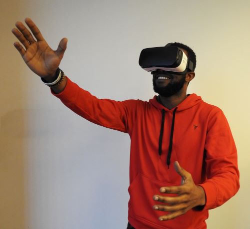 Photo of smiling man in hooded sweatshirt wearing virtual reality headset and extending hand