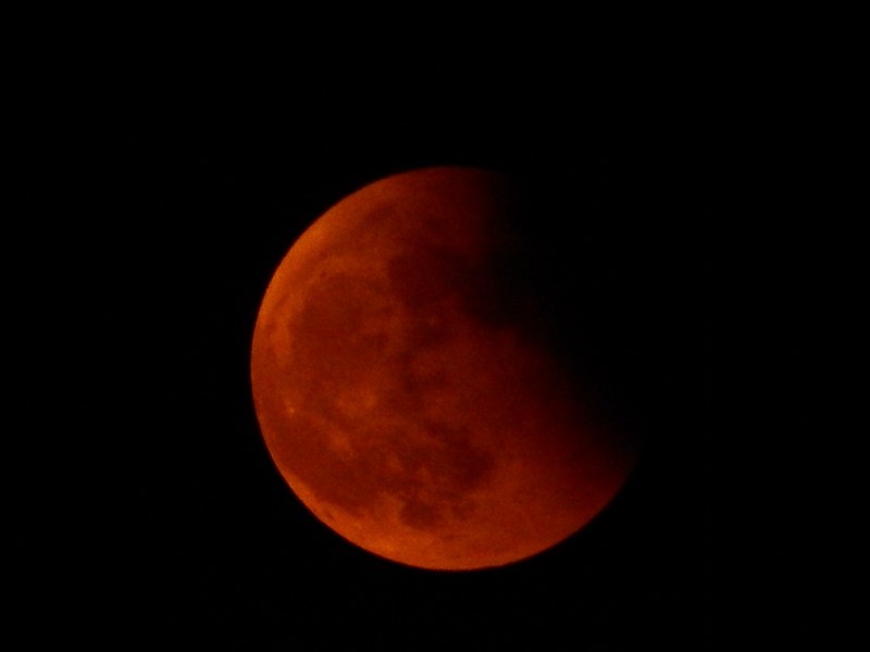 Red-tinged blood moon, partly visible against black night sky