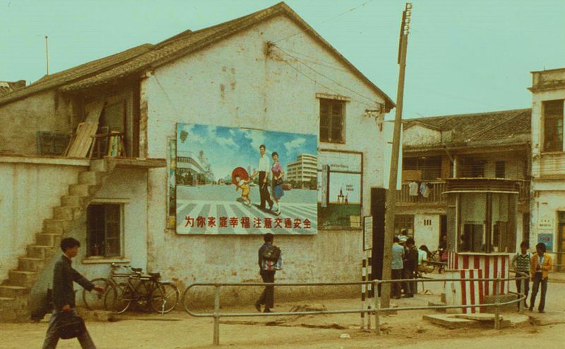 People walking past a 1980s Chinese poster on a street depicting a modern family and suggesting economic prosperity