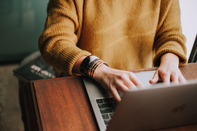 Person from neck down facing forward and with hands on laptop keyboard