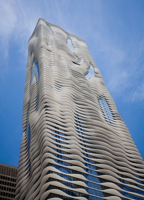 Photo of a tall building against blue sky, with architecture that creates an undulating effect