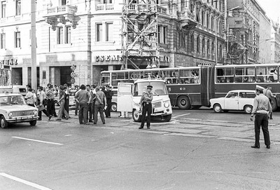 Black-and-white photo of people standing in a street with buses and cars in the background