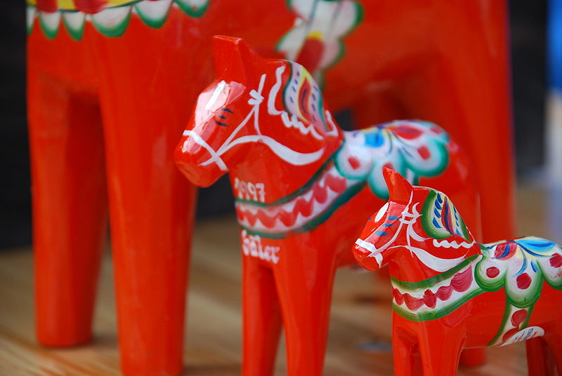 Three wooden Dala horse figurines of different sizes, painted orange-red with additional ornate decorative patterns