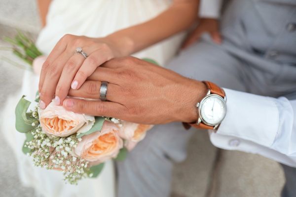 Photo of a couple's hands over a wedding bouquet