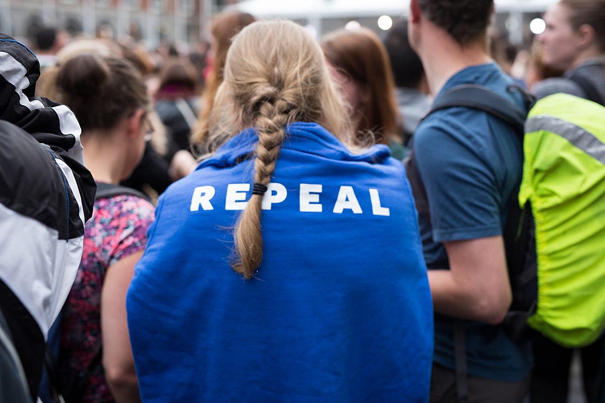 Photo of crowd in London after repeal of abortion ban, with central focus on the back of a blue item of clothing reading 'Repeal' in white letters