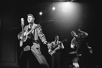 A black and white photo of Elvis performing with two other band members