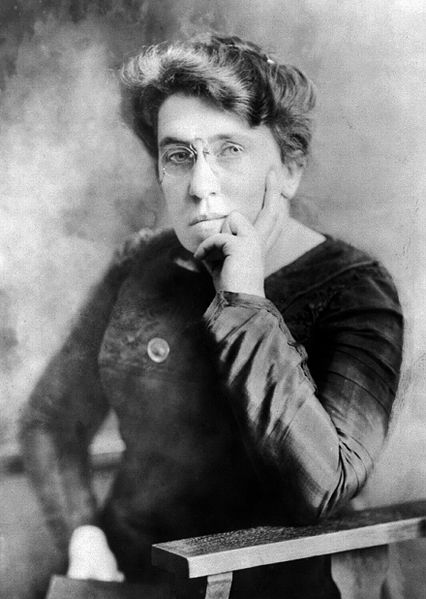 Black-and-white photo portrait of Emma Goldman, seated with book against indistinct background
