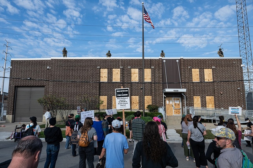 ICE facility in Chicago with guards on the roof and boarded up windows and protesters on the ground