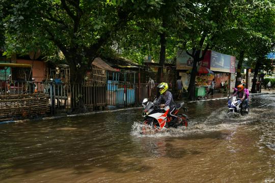 Three people drive motorcycles through a flooded street