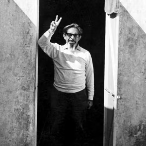 Black and white photo of José Revueltas standing outside holding up a peace sign