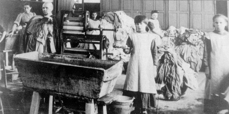 Young girls stand in front of a manual washing machine