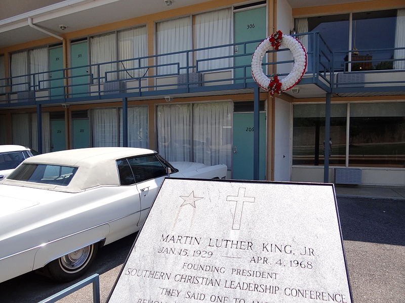 Photo of the Lorraine Motel in Memphis, site of MLK's assassination, with commemorative plaque in foreground and red-and-white wreath visible on the balcony