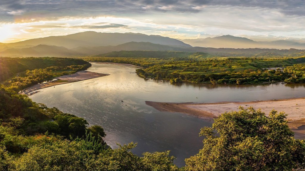 Magdalena River at sunset with tree-lined banks and mountains in the distance