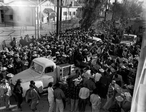 Black-and-white photograph of a crowd of workers standing in a street