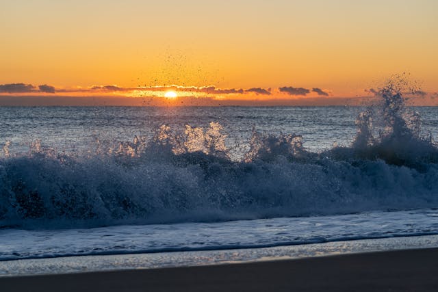 Waves of the ocean against the shore with a sunet in the background
