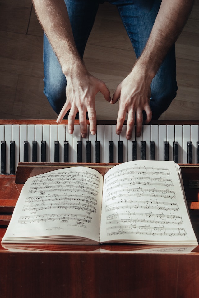 Photograph from above showing arms and hands of pianist playing piano with sheet music