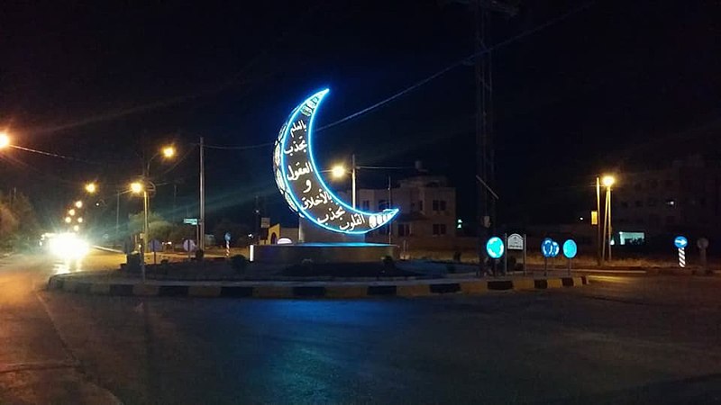 Nighttime photograph of a crescent moon statue lit with neon light in Jordan for the celebration of Ramadan