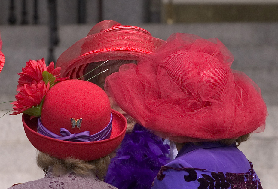 Three members of the Red Hat Society of Victoria, British Columbia wearing formal purple clothes and red hats as they face one another