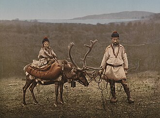 A man herds a reindeer while a young child sits on it