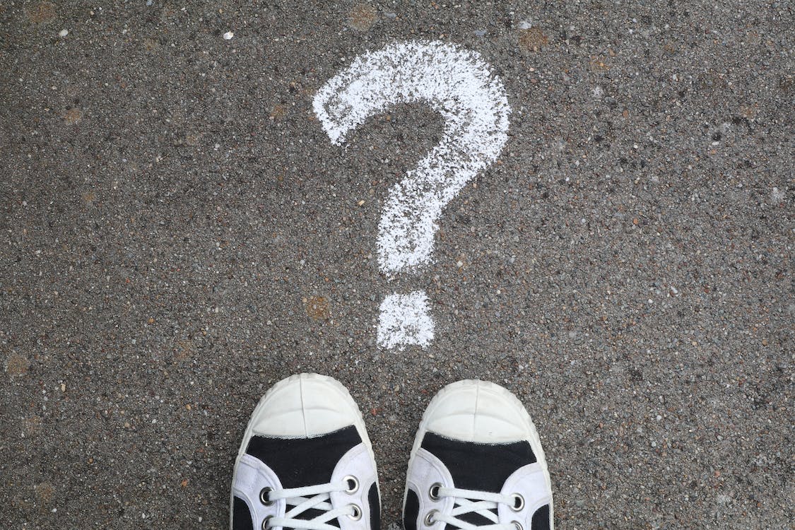 Question mark drawn in chalk on pavement above a pair of black-and-white sneakers