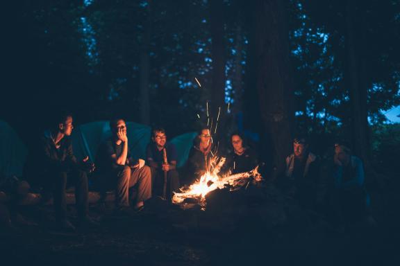 A group of people sit around a campfire in the woods