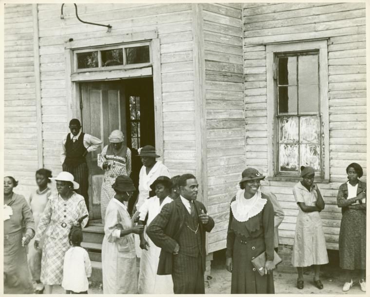 Black-and-white photo of churchgoers standing outside in formal attire