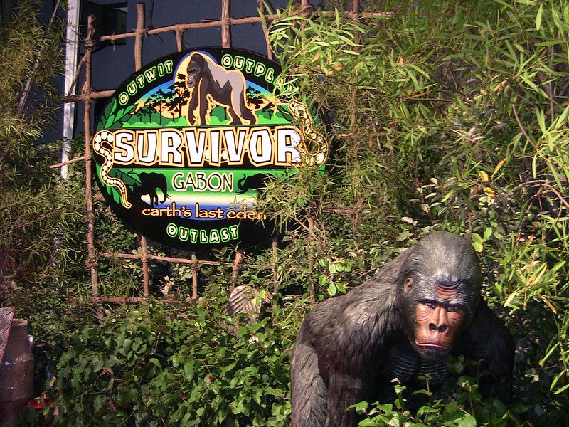 Photo of a promotional scene for Survivor in Gabon, including a sign advertising the show and a gorilla statue surrounded by foliage