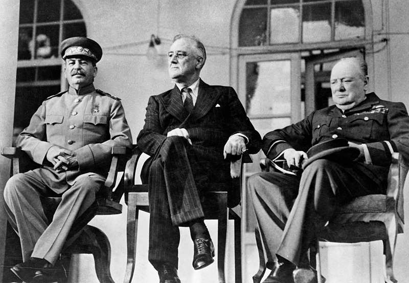 Black-and-white photograph of Stalin, Roosevelt and Churchill seated in a row at the Tehran Conference