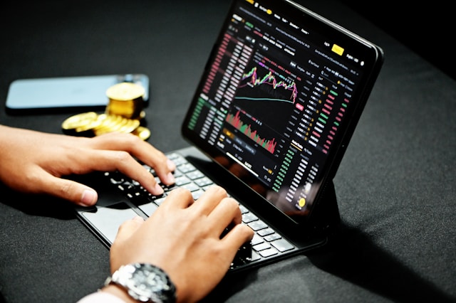 A person sits at a laptop as the screen shows a currency trading market