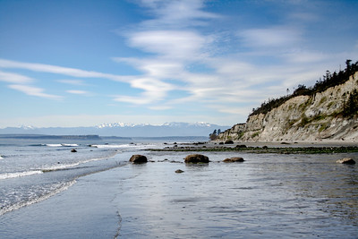 Photo of a rock-strewn shore on a clear day with mountains visible in background